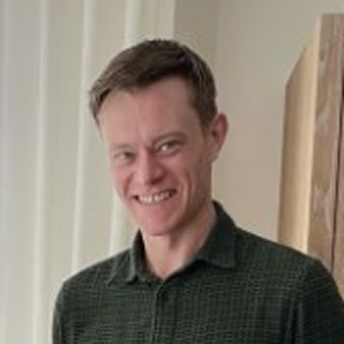 Portret van jongere man met kort haar, glimlachend, in grijs overhemd.