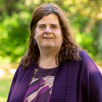Portret van vrouw met halflang donker haar en paarse trui buiten in groen decor.