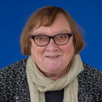 Portret van oudere vrouw met bril, kort haar en lichte sjaal voor blauwe achtergrond.