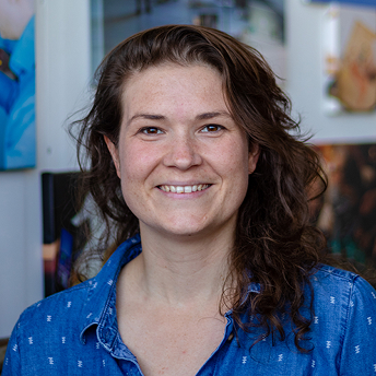 Portret van vrouw met donker krullend haar in blauwe blouse.